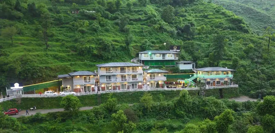 A white resort building set into a forested Mussoorie hillside